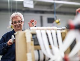 eine ältere Dame arbeitet an einer Falzmaschine. 