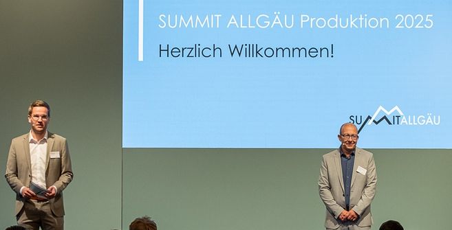 Zwei Herren stehen vor einer Leinwand beim Summit Allgäu Produktion 2025.